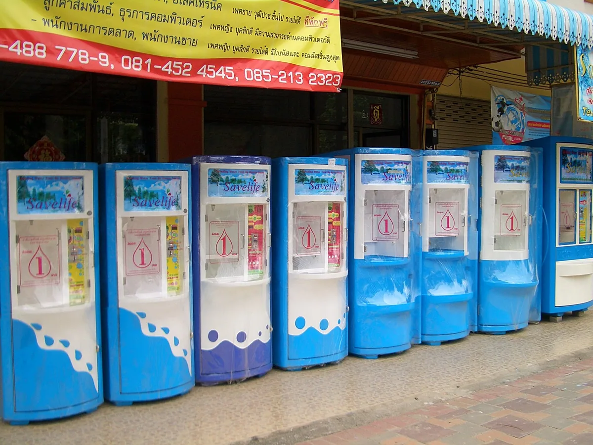 A row of blue-and-white coin-operated drinking water refill machines on a pavement in Pattaya