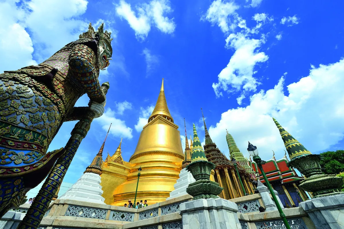 Gold-covered Phra Si Rattana chedi and gilded spires at Wat Phra Kaew in Bangkok under a blue sky