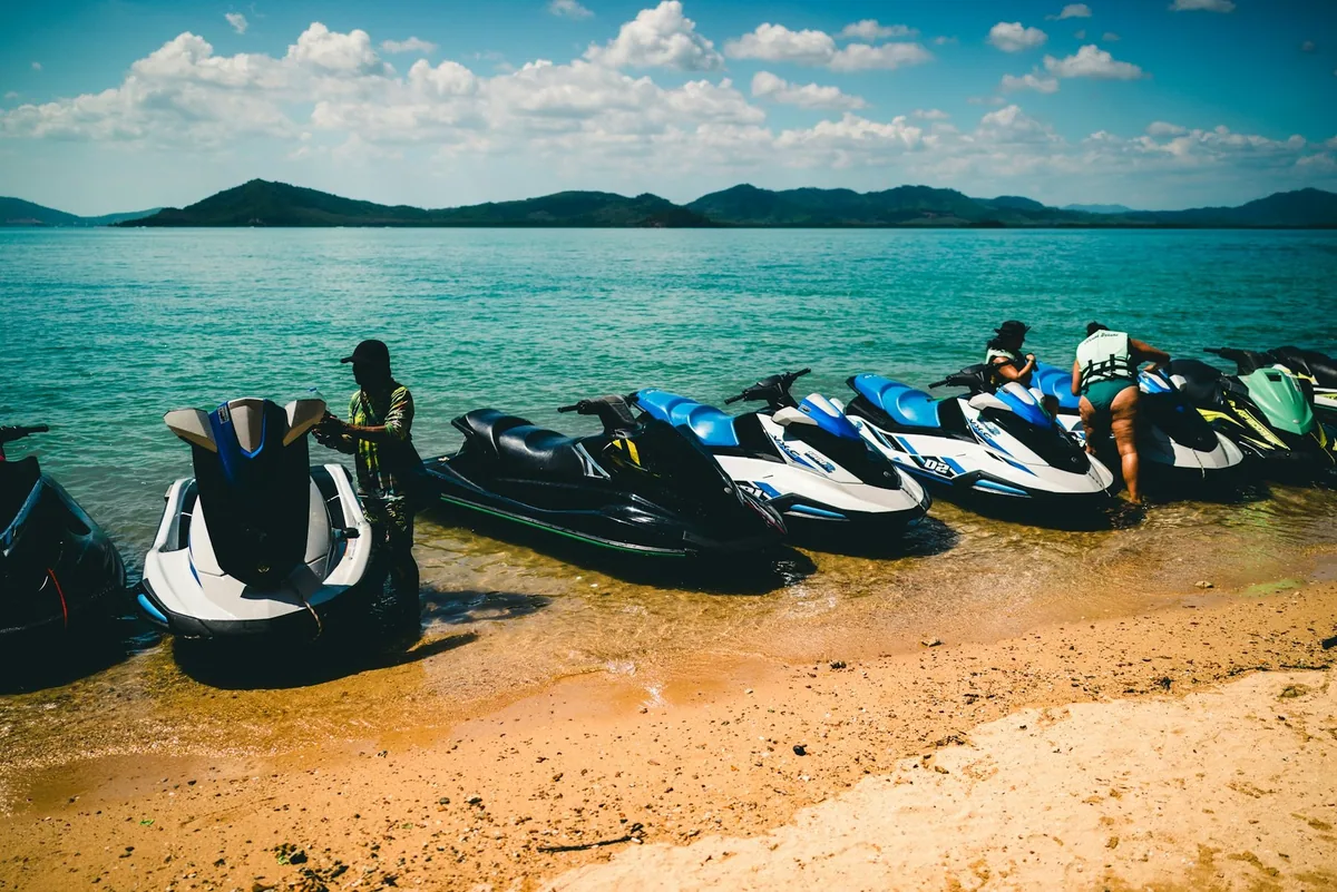Rental jet skis lined up on the sand at the water's edge of a Phuket beach