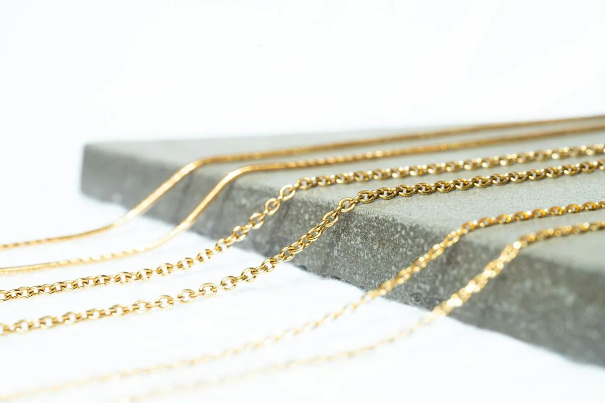Several plain gold chains in different link styles draped over the edge of a grey stone slab