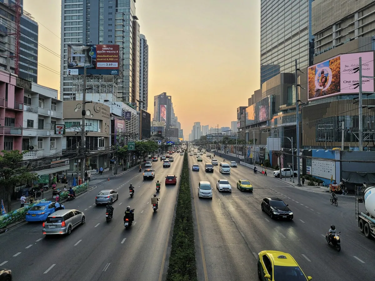 Cars and motorbikes on a wide multi-lane avenue between Bangkok shopping malls at sunset