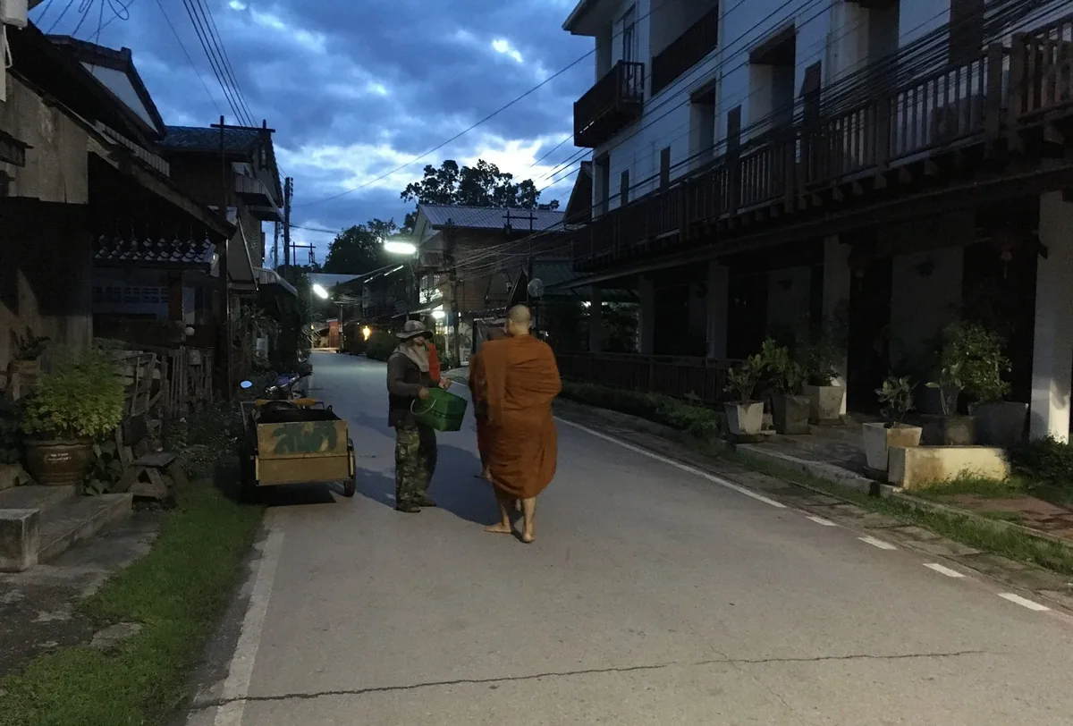 Monk in saffron robes walking the morning alms round past wooden shophouses in Chiang Khan