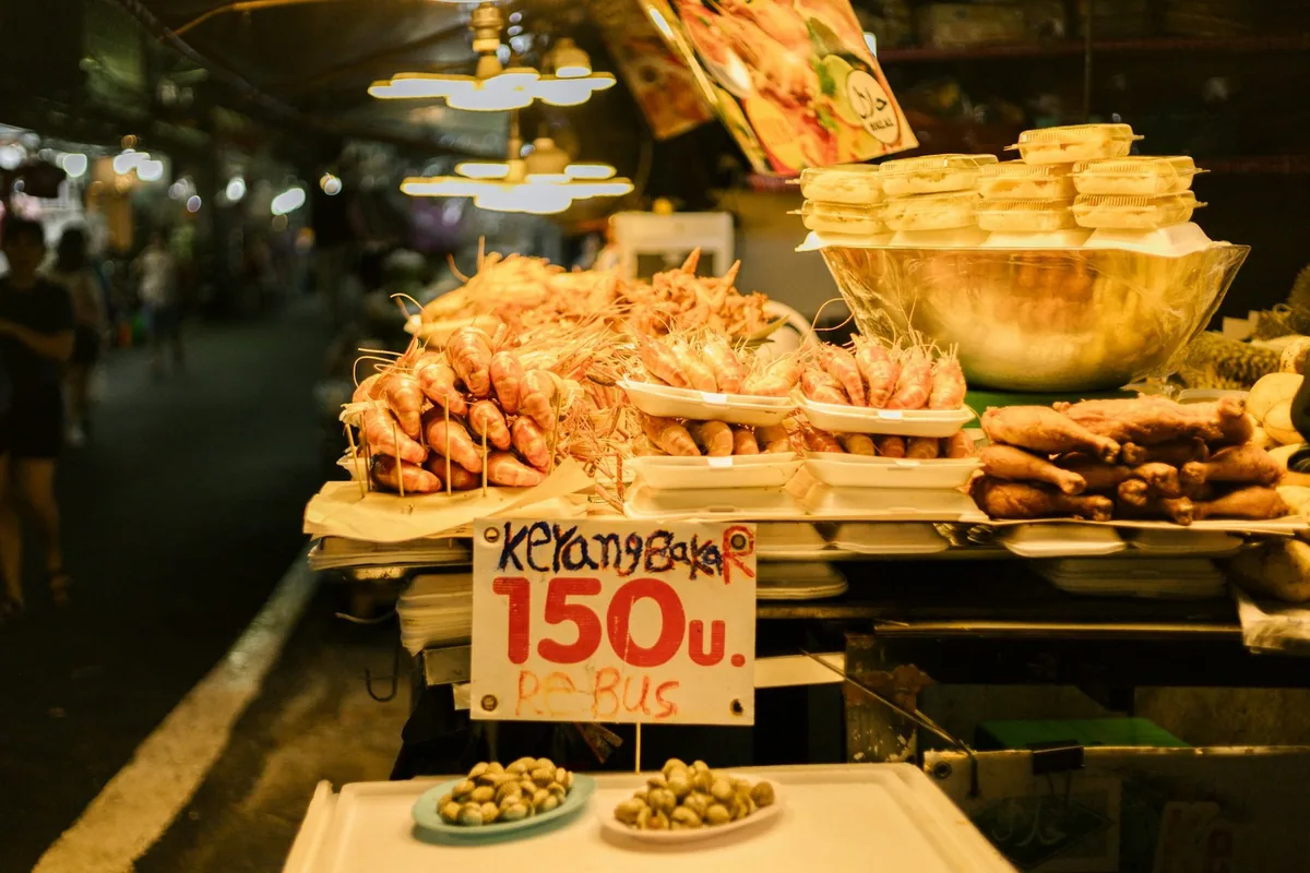 Fried shrimp and crispy snacks piled high on a lamp-lit night market stall with a price sign