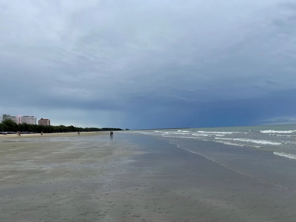 Dark rain clouds gathering over the sand and surf of Hua Hin beach