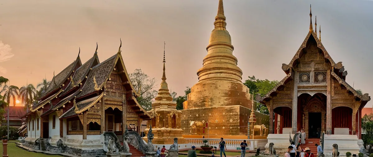 Golden chedi and carved Lanna-style halls of a Chiang Mai temple glowing in evening light