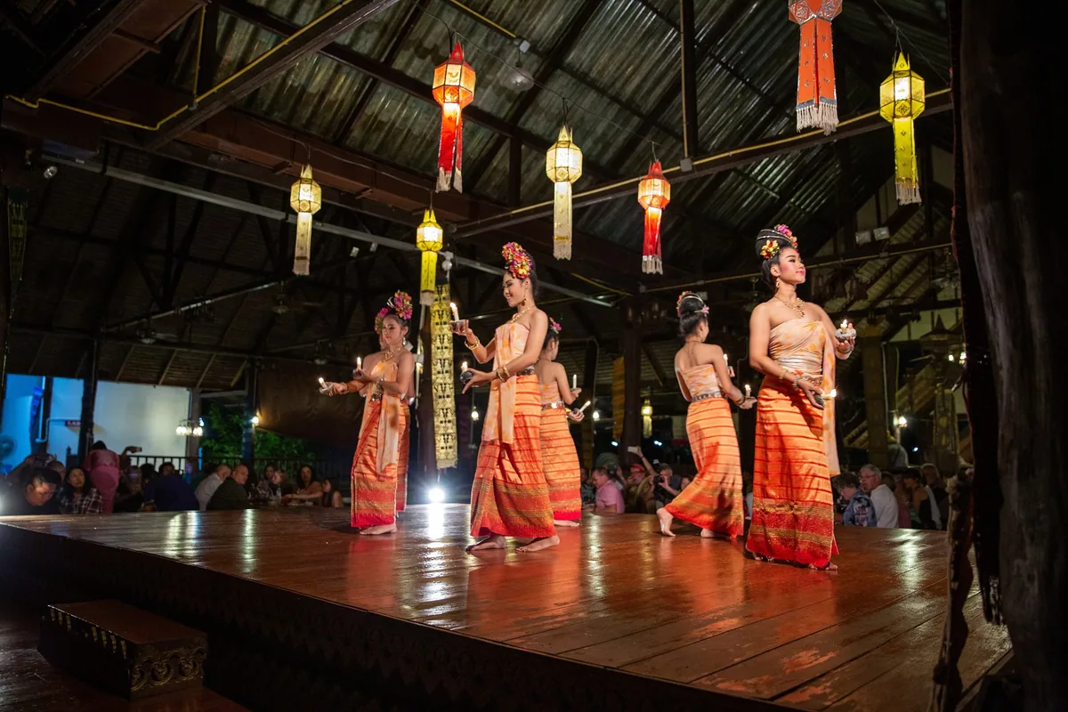 Dancers in orange Lanna costume perform on a wooden stage under paper lanterns at a khantoke dinner in Chiang Mai