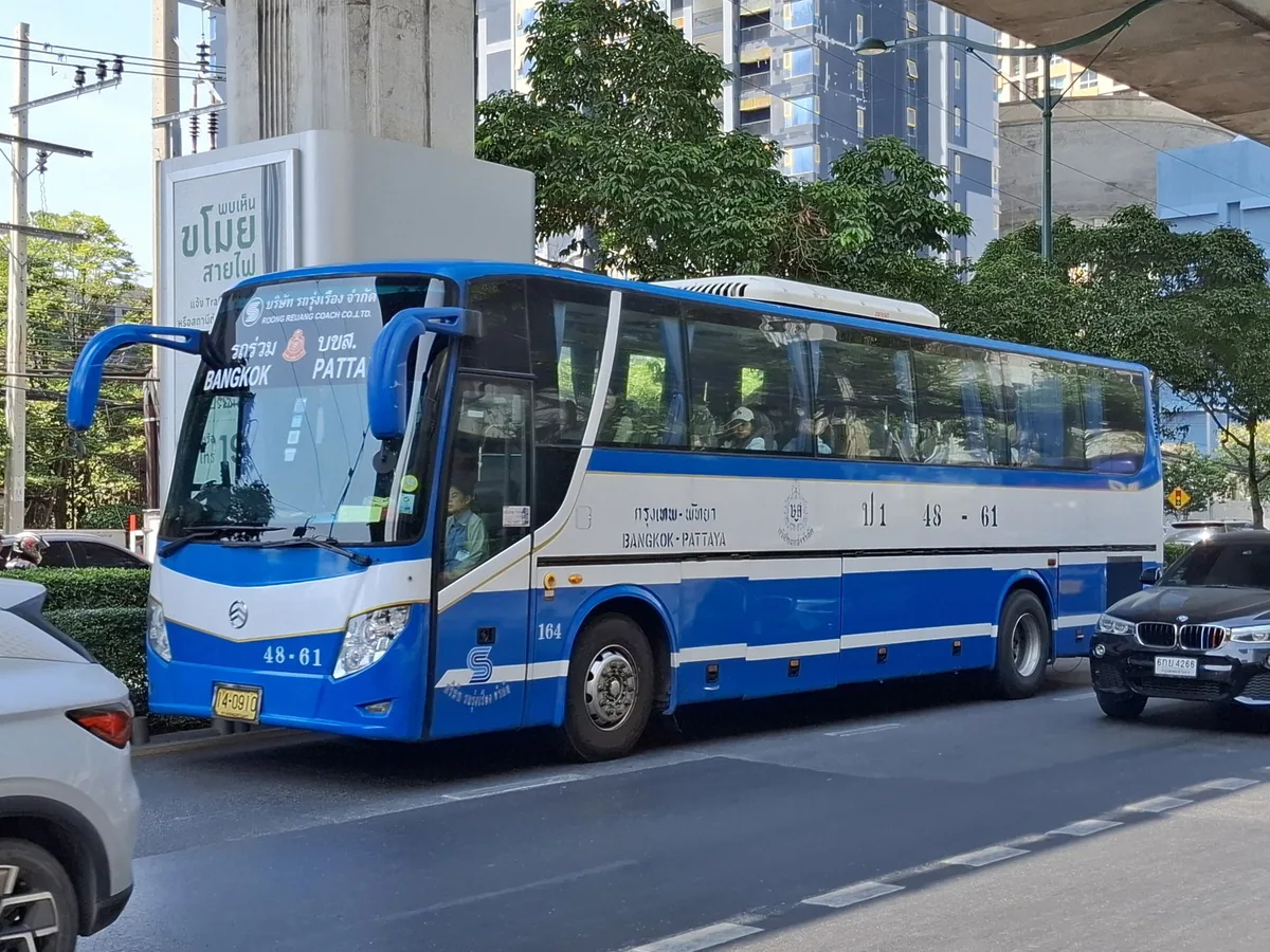 Blue and white Bangkok–Pattaya intercity bus waiting at a stop under an elevated road in Bangkok