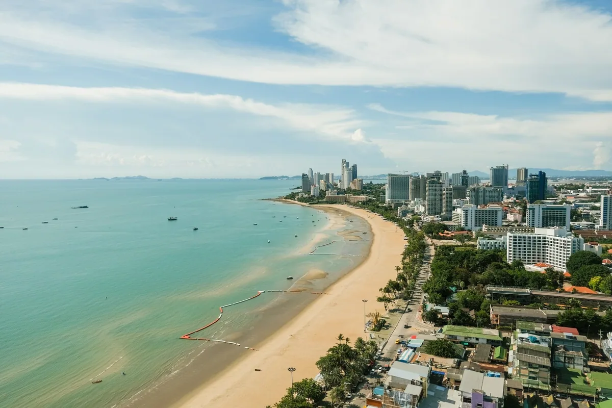 Aerial view of a long curving sandy beach in Pattaya backed by hotels and apartment towers