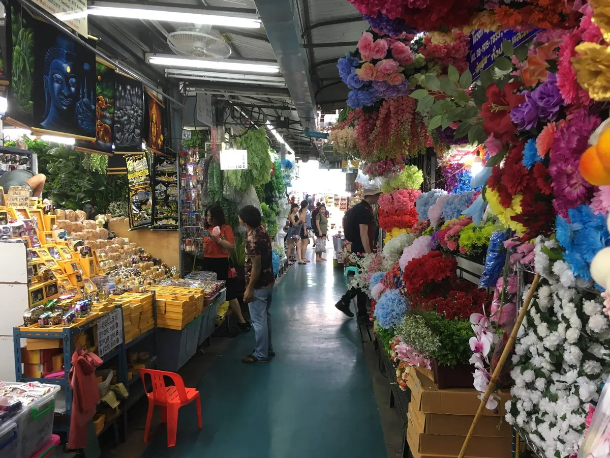 Covered aisle at Chatuchak Weekend Market lined with artificial flower and snack stalls