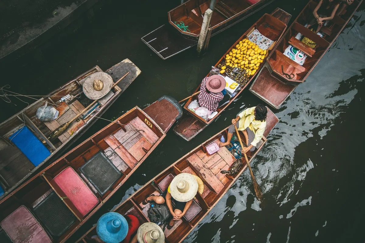 Vendors in straw hats paddling wooden boats loaded with fruit at Damnoen Saduak floating market