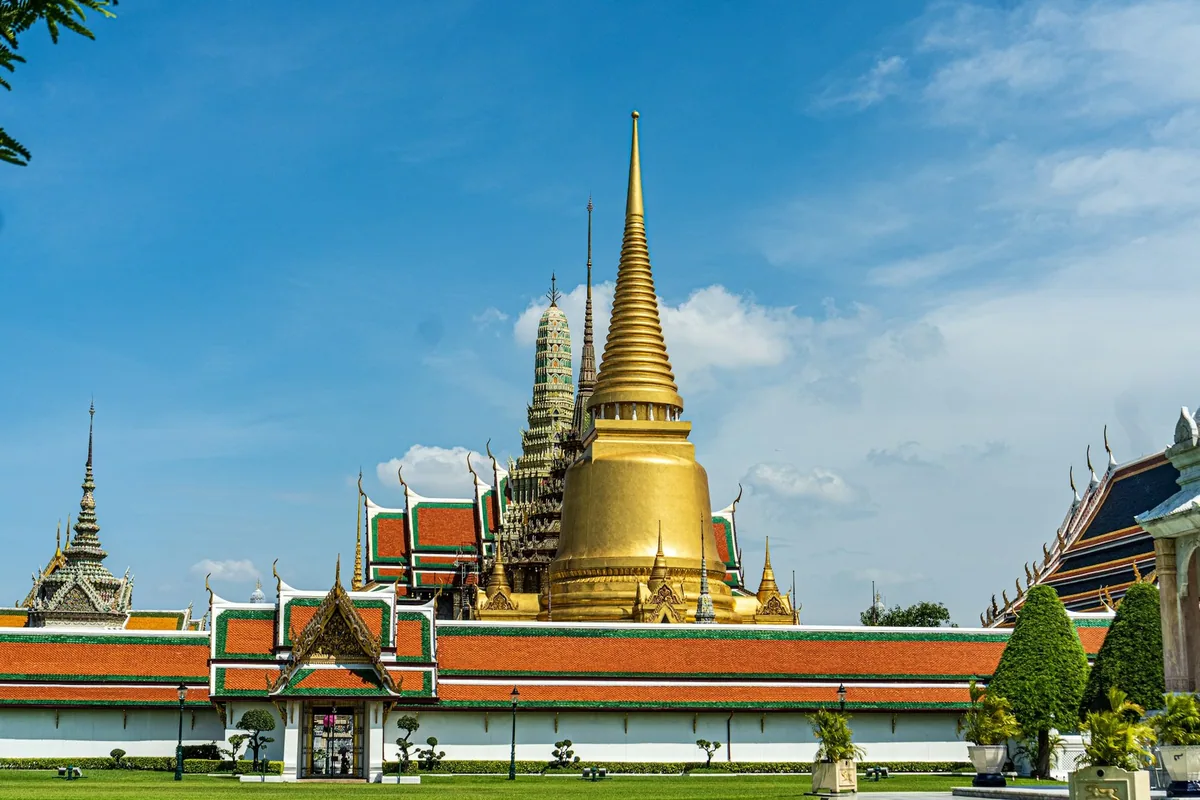 Golden chedi and red-tiled roofs of Wat Phra Kaew behind the Grand Palace wall in Bangkok