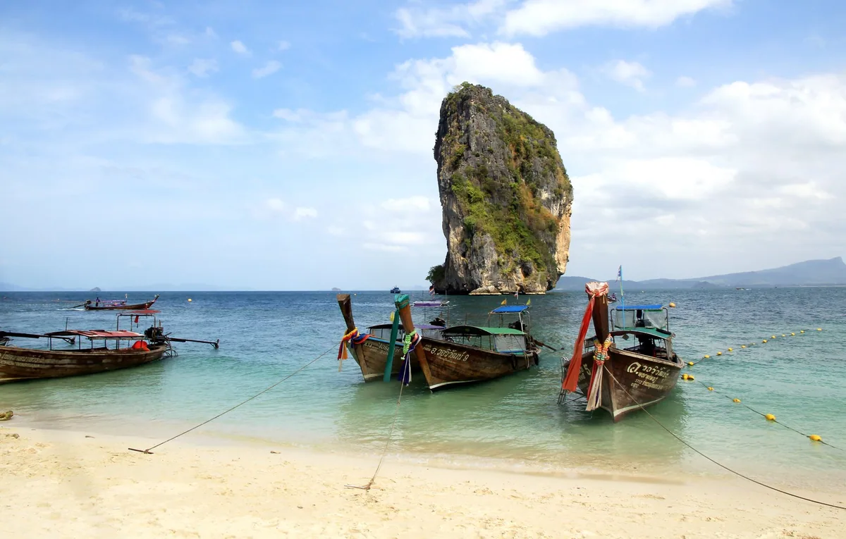 Longtail boats moored off Ko Poda beach in front of the tall limestone rock of Ko Ma Tang Ming