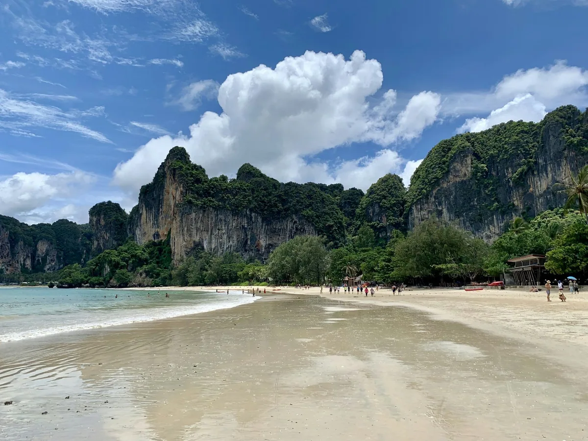 Sandy Railay Beach with swimmers below towering green limestone cliffs under a blue sky