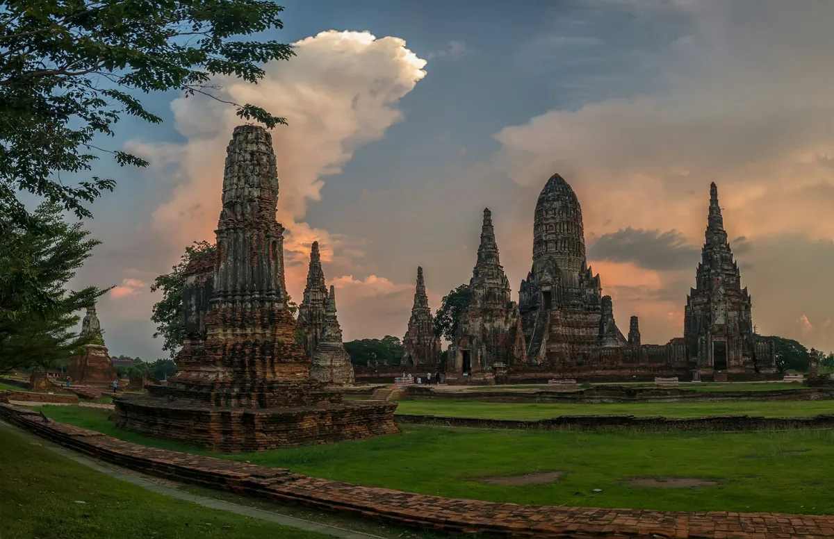 The Khmer-style prangs of an Ayutthaya temple ruin under dramatic evening clouds