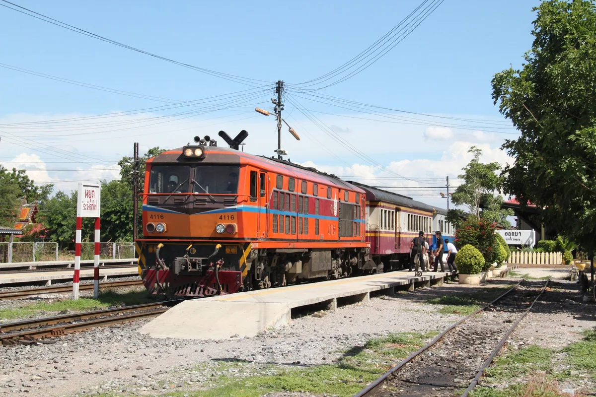 Orange diesel locomotive pulling a passenger train into Ayutthaya railway station