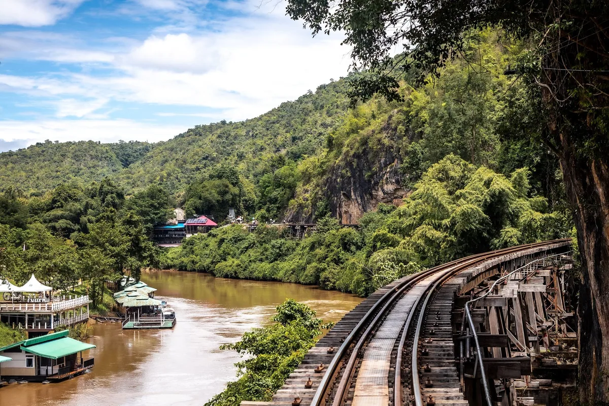 Death Railway viaduct clinging to a cliff above the River Kwai, with raft houses moored below