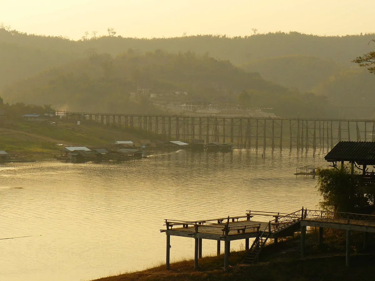 The wooden Mon Bridge stretching across Khao Laem Lake at Sangkhlaburi in hazy golden evening light