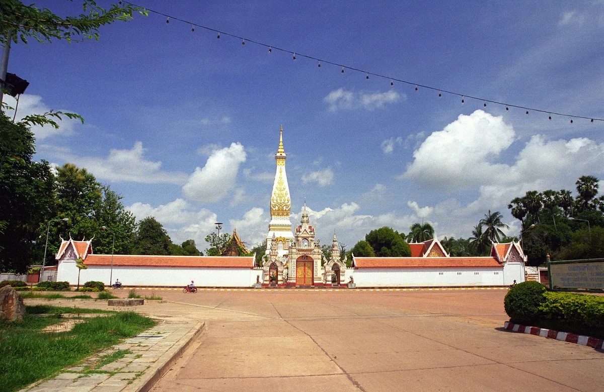 The white and gold stupa of Wat Phra That Phanom rising behind the temple's red-roofed outer wall in That Phanom