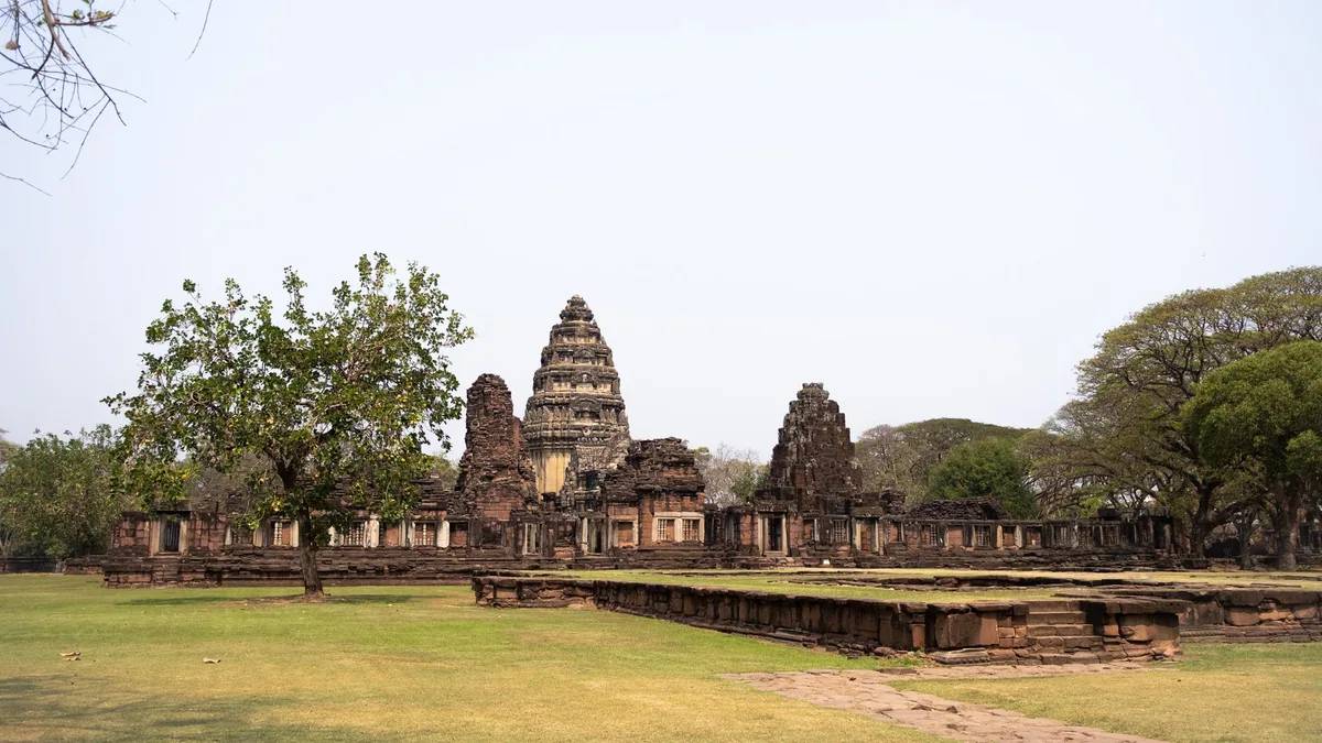 The sandstone towers of Prasat Hin Phimai rising behind its enclosure wall and lawns in Phimai Historical Park