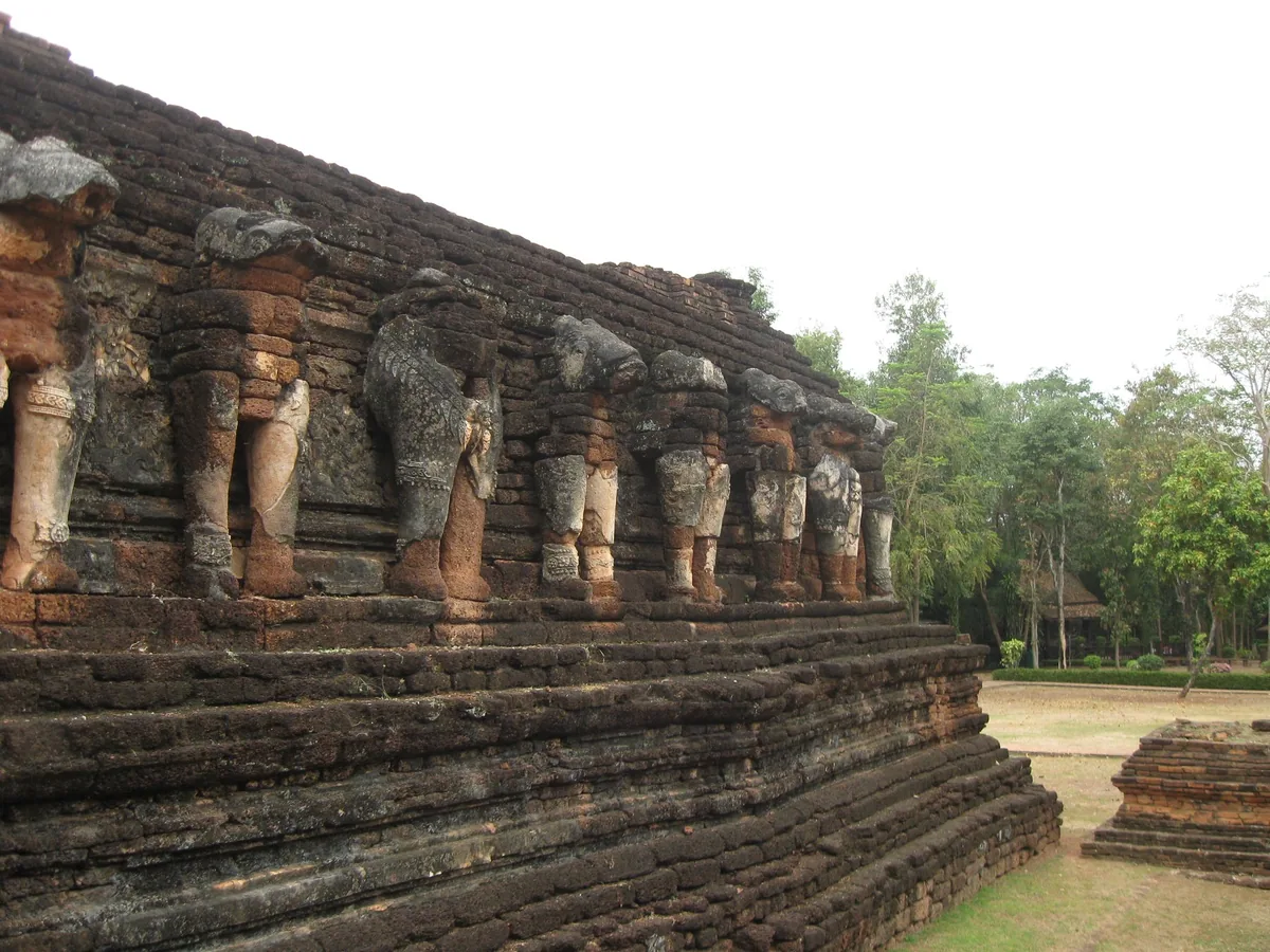 Row of weathered elephant sculptures around the laterite base of Wat Chang Rop in Kamphaeng Phet Historical Park