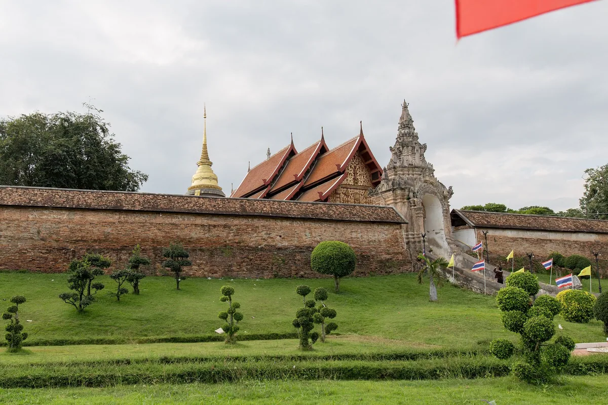 Brick walls, golden chedi and tiered Lanna roofs of Wat Phra That Lampang Luang above its clipped-hedge lawn