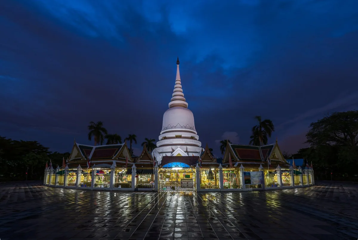 The white chedi of Wat Phra Mahathat in Nakhon Si Thammarat lit up at dusk under a deep blue sky