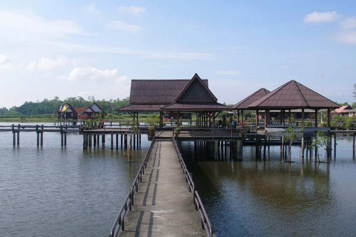 A long walkway leading to wooden pavilions on stilts over the open water of Thale Noi lake in Phatthalung