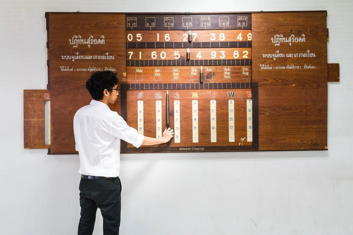 A man sets the sliding wooden panels of M.L. Pin Malakul's perpetual Thai solar calendar, labelled in Thai and English