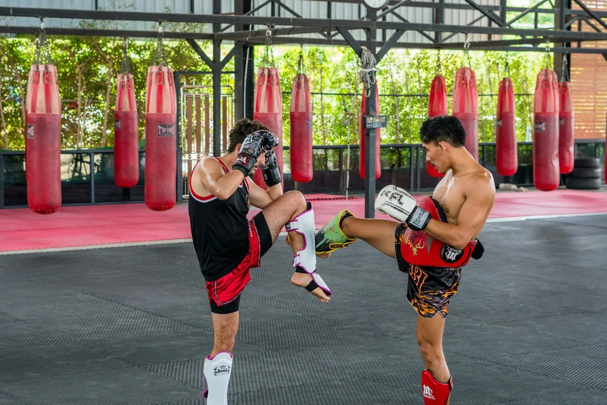 Two fighters practising knee strikes in an open-air Muay Thai gym lined with red heavy bags
