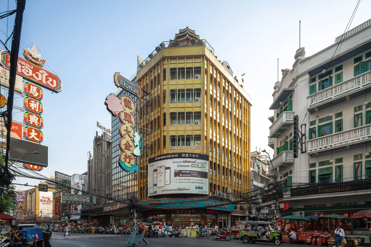 Gold shop signs and a gold-trading billboard on a yellow tower above Yaowarat Road in Bangkok's Chinatown