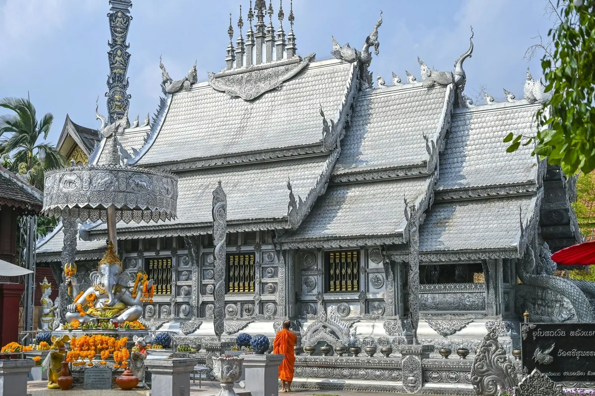 A monk in saffron robes walks past the silver ordination hall of Wat Sri Suphan in Chiang Mai