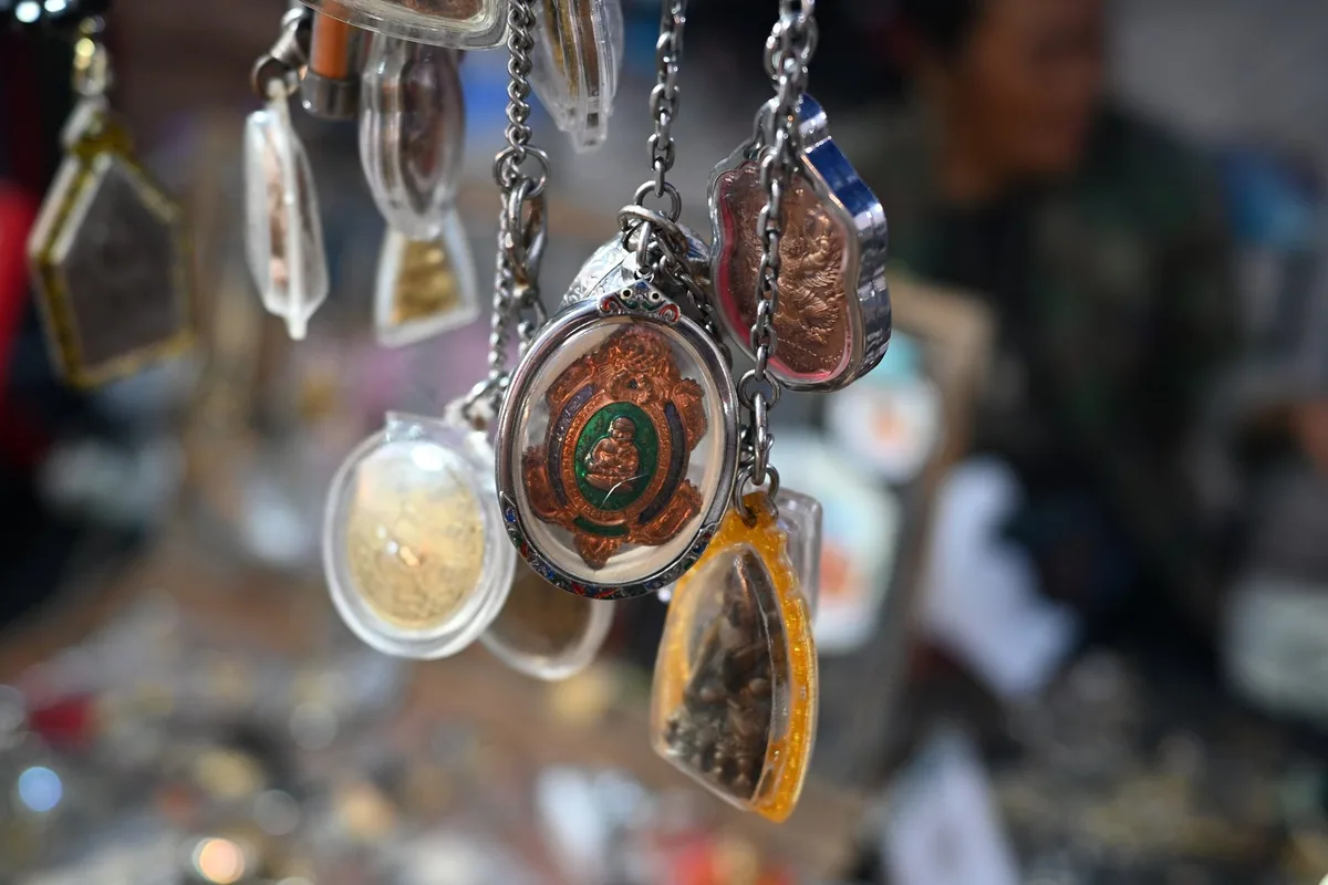 Thai Buddhist amulets in clear resin and metal casings hanging on chains at a market stall