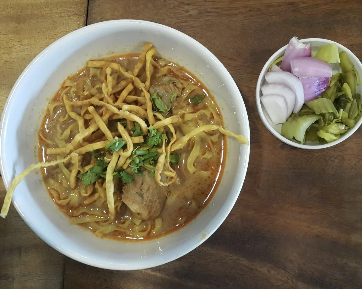 Bowl of khao soi curry noodles with crispy noodles, shallots and pickled greens in Chiang Mai