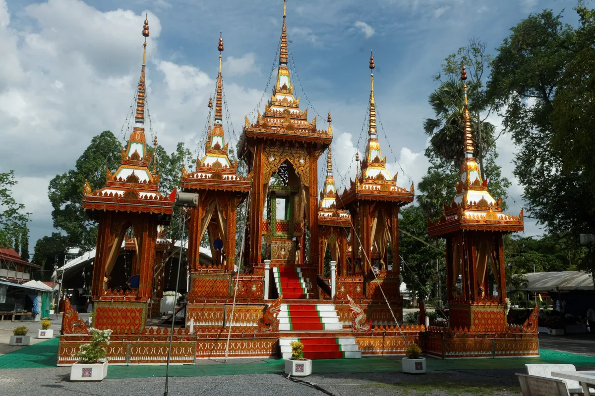 Ornate red and gold temporary cremation pavilion with tiered spires in the grounds of Wat Phatthanaram, Surat Thani