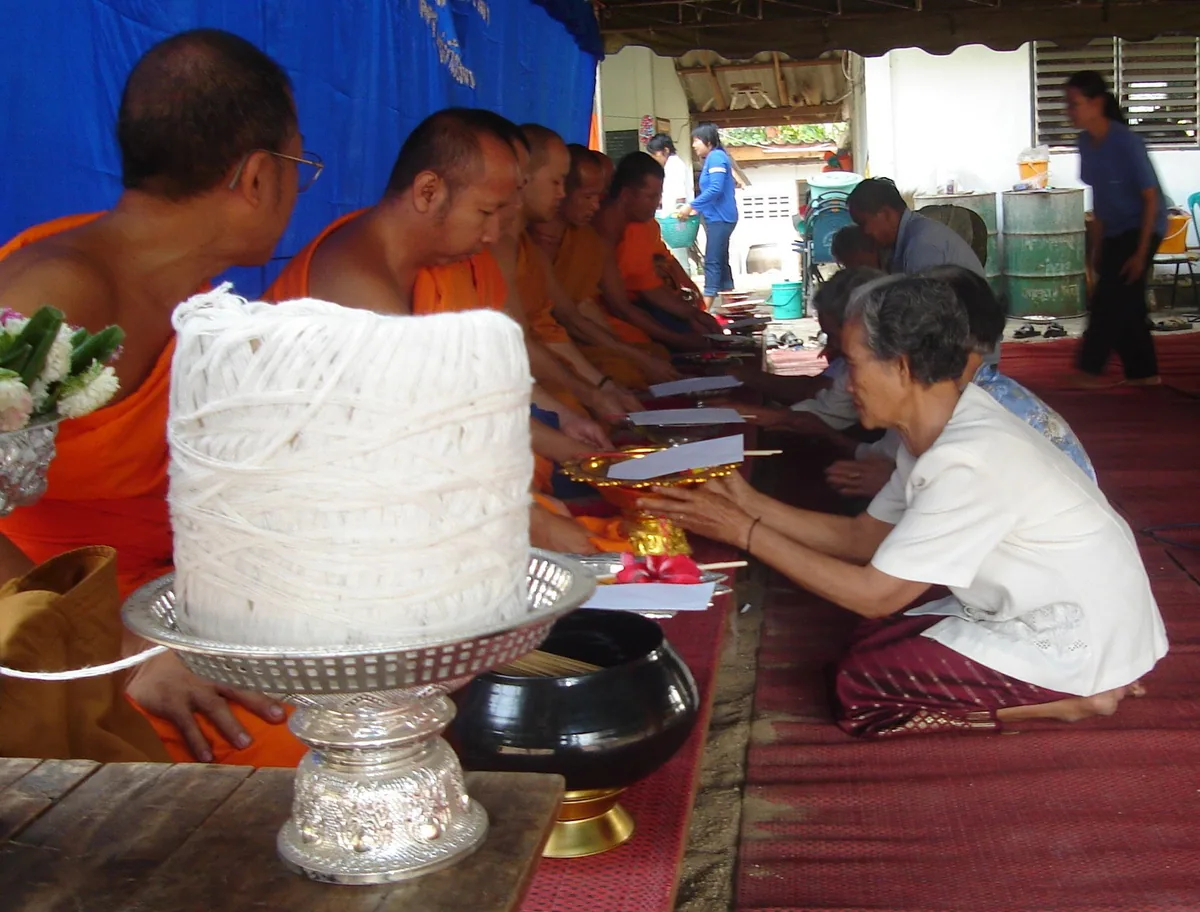 A spool of white sacred thread on a silver tray as lay people present offerings to a row of seated monks