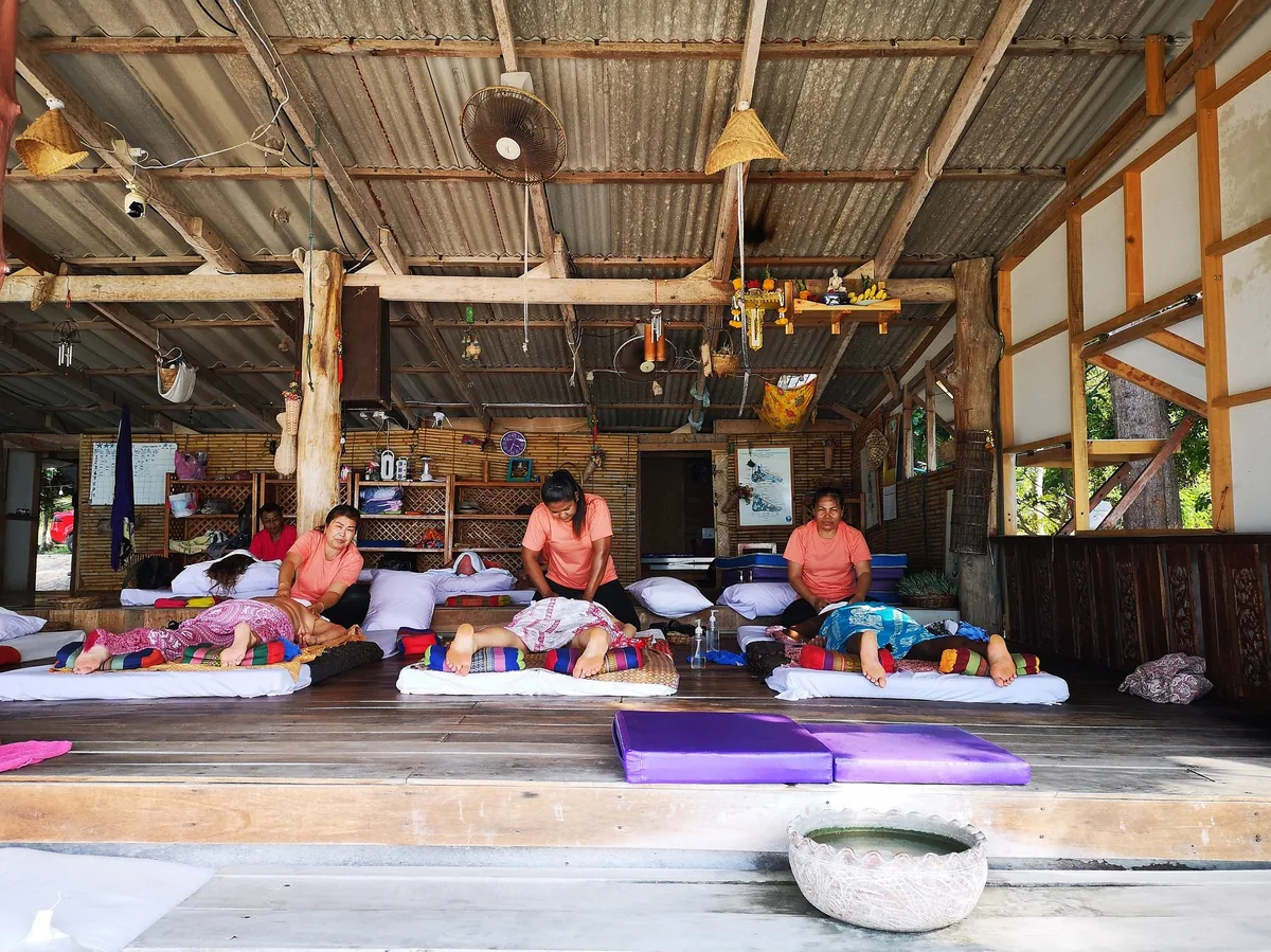 Therapists giving traditional Thai massage on floor mats in an open wooden massage hall