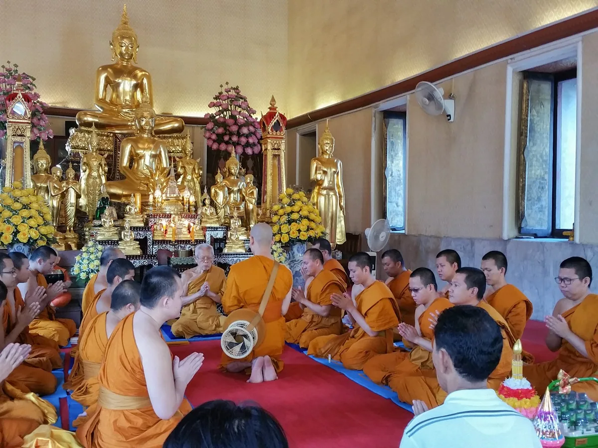 Monks seated in a temple hall at Wat Yannawa, Bangkok, as a newly robed candidate kneels before the preceptor