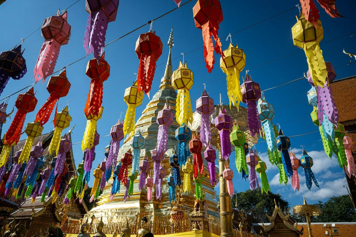 Colourful Lanna paper lanterns strung in front of a golden chedi in Chiang Mai