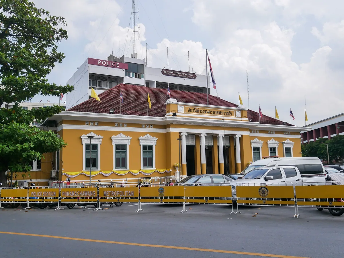 Yellow colonial-style front of Phra Ratchawang Metropolitan Police Station in Bangkok behind police barriers