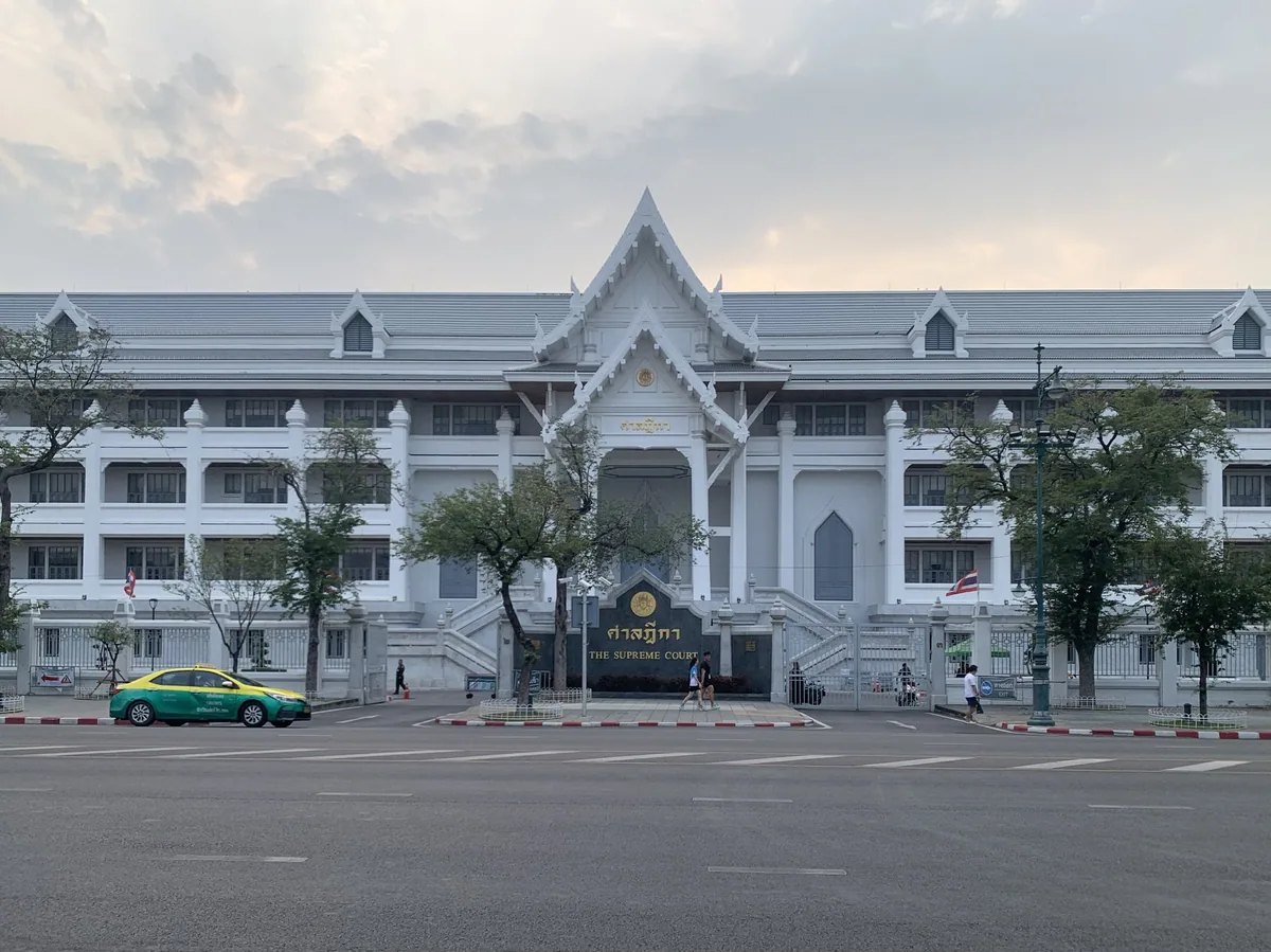 The white facade of the Supreme Court of Thailand building in Bangkok behind a row of trees