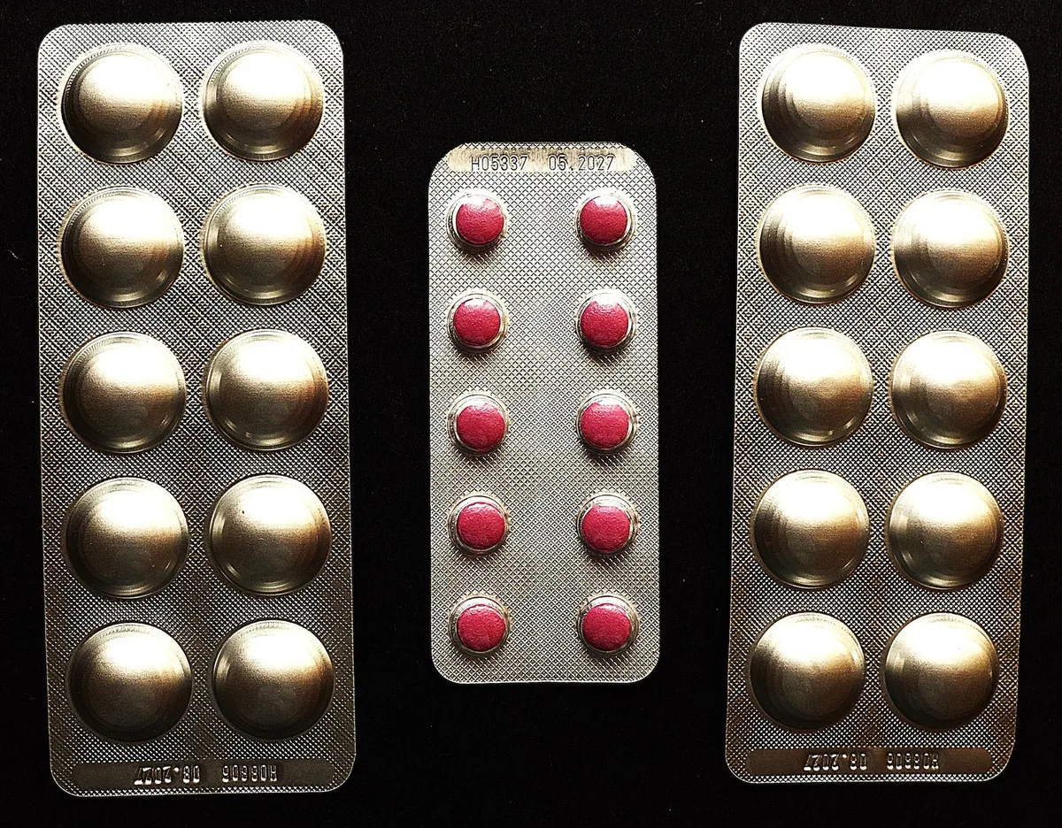 Three blister strips of round tablets, gold and red, laid out on a black background