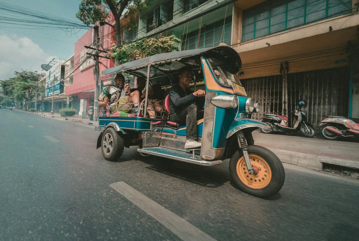 Passengers riding in a colourful tuk-tuk through a Bangkok street