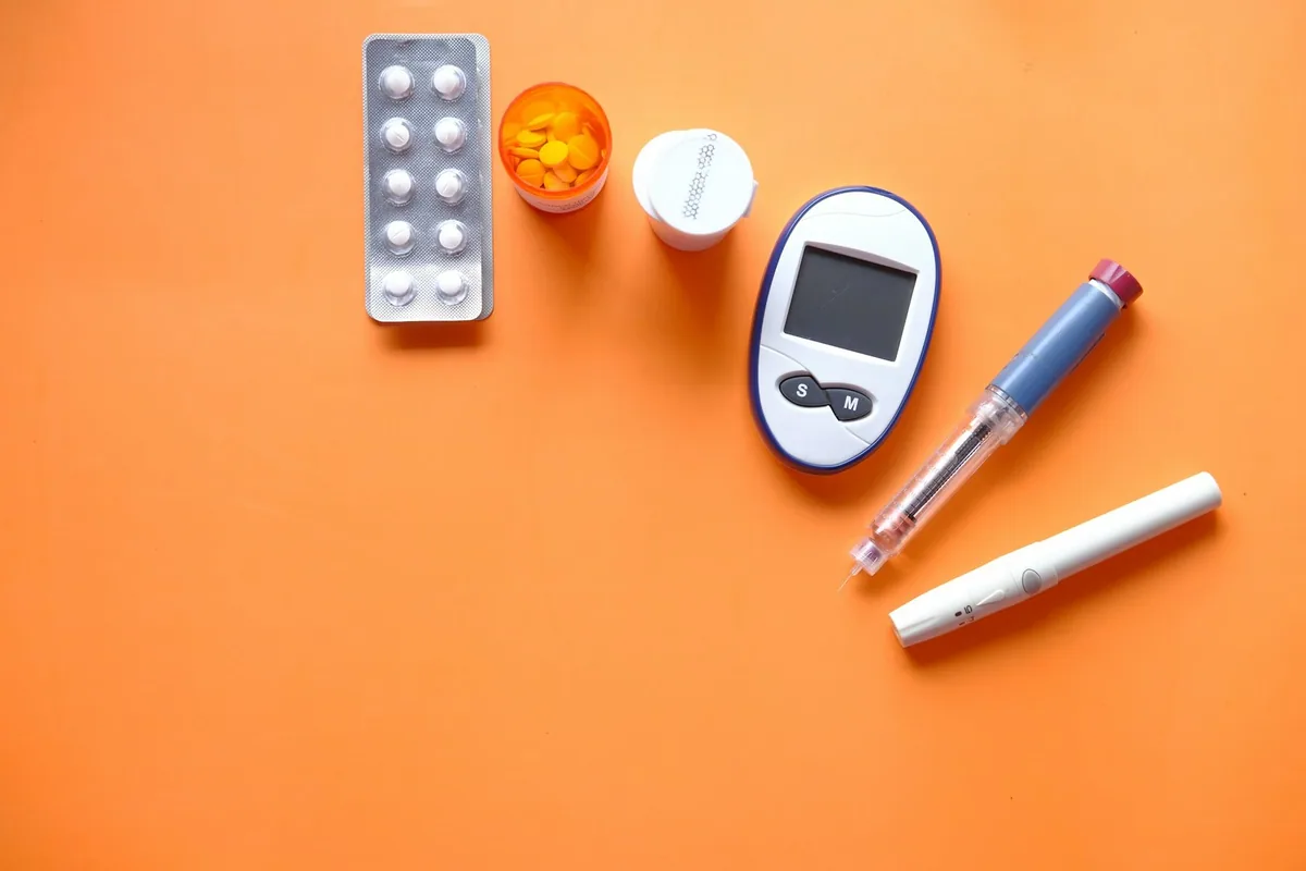 Insulin pen, blood glucose meter, lancing device and tablets laid out on an orange surface
