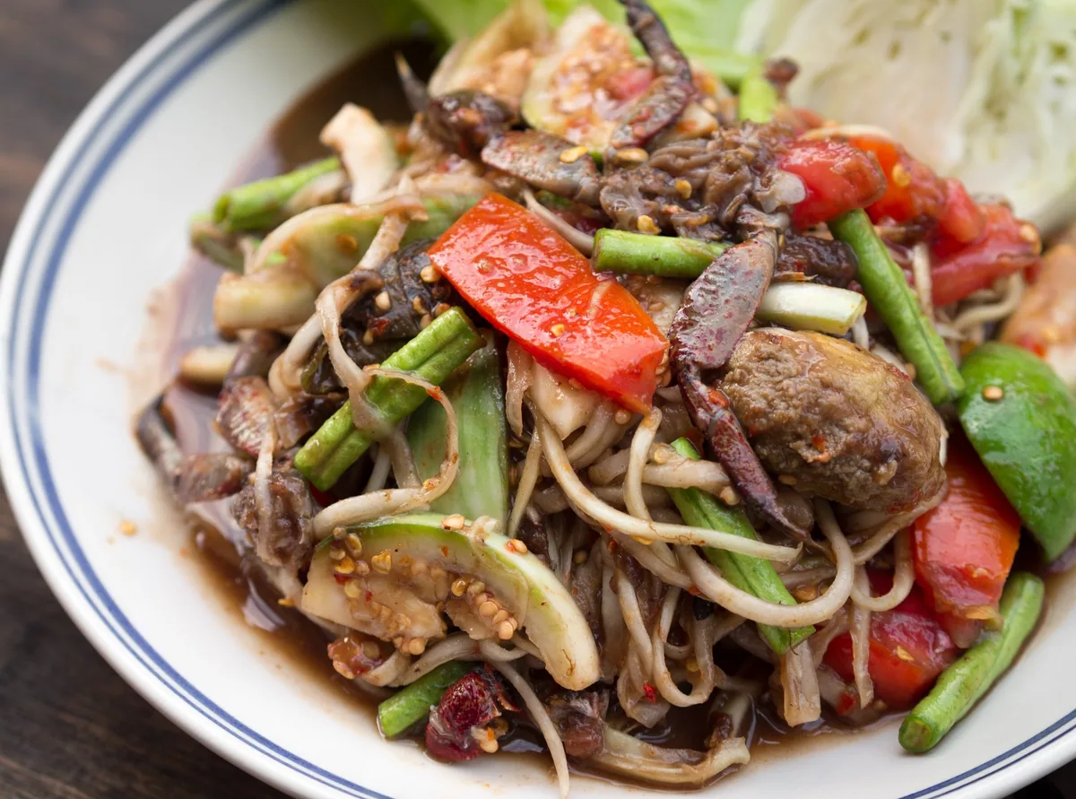 Plate of dark som tam Lao, papaya salad made with fermented pla ra fish, pickled crab, chillies, beans and tomato