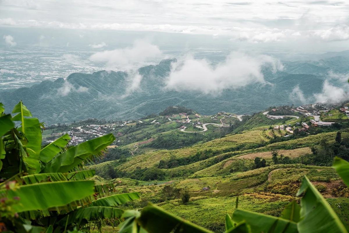 A road twisting in tight curves through hillside villages below misty mountains in the Thai highlands