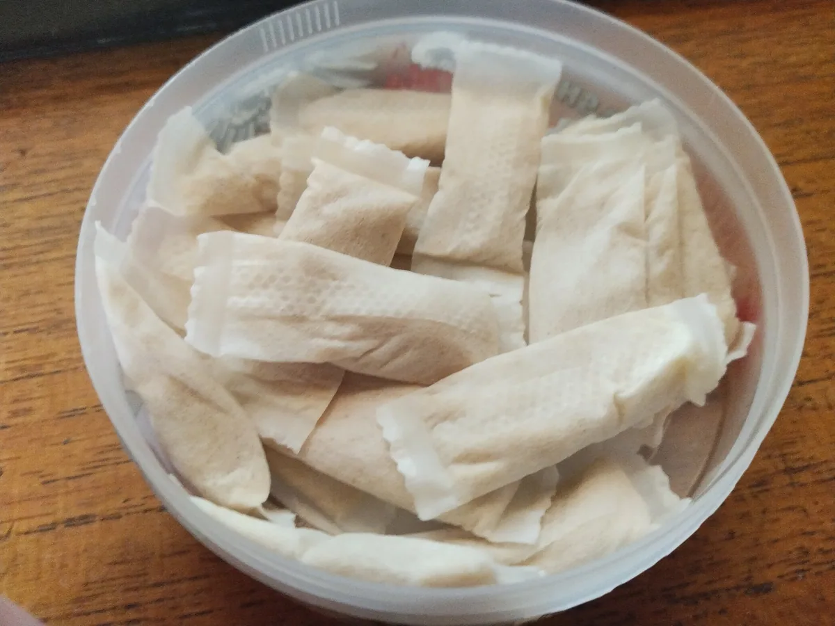 An open tub full of white nicotine pouches on a wooden table