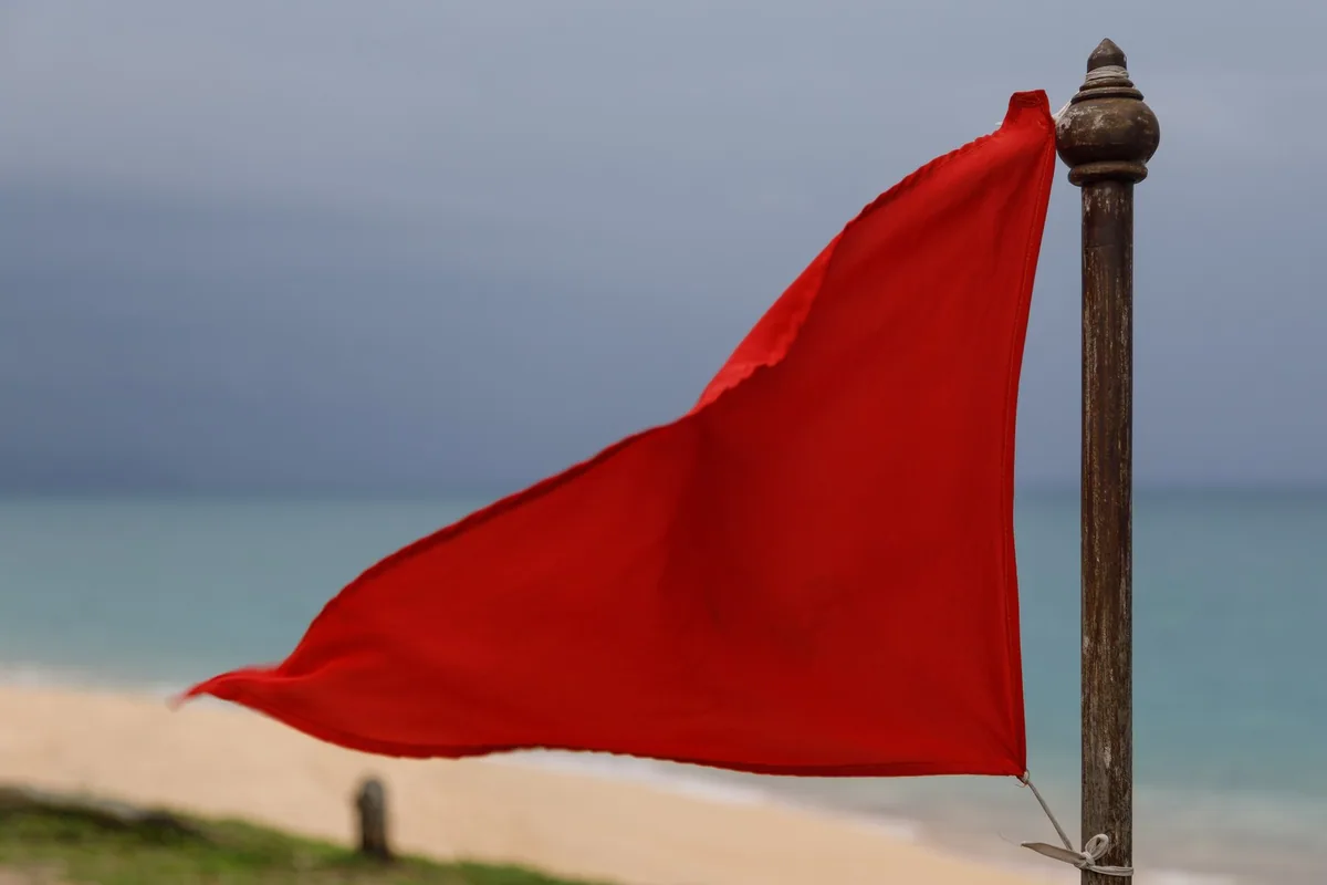 Red no-swimming warning flag flying on Mai Khao Beach, Phuket, under a grey monsoon sky