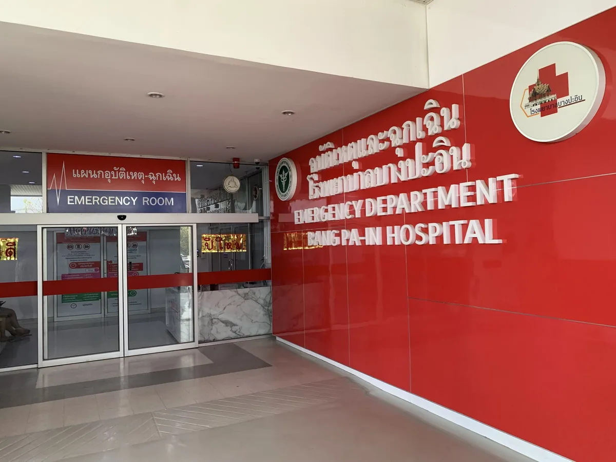 Glass doors of the emergency department at Bang Pa-in Hospital beside a red wall with bilingual signage