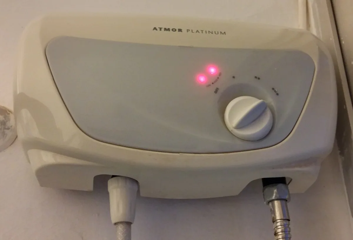 Wall-mounted electric instant water heater with a power dial, indicator lights and hoses to the shower
