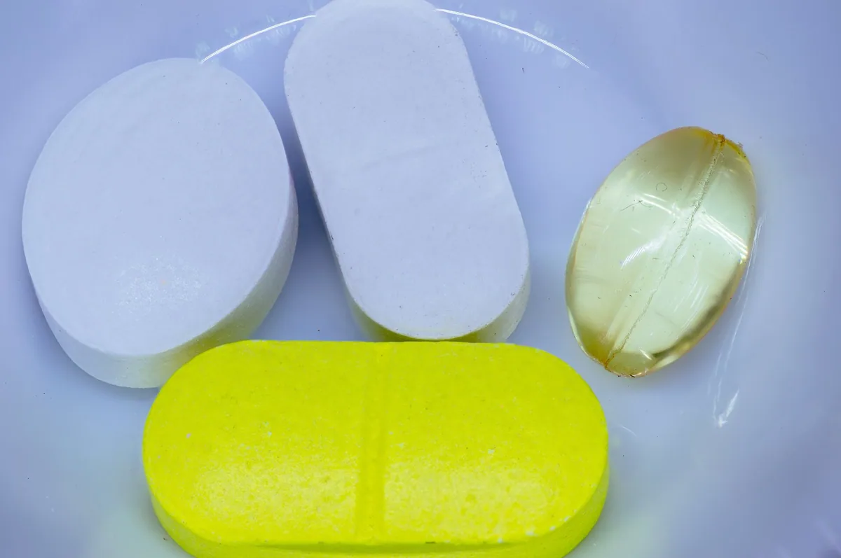 Close-up of large white and yellow tablets and a clear gel capsule in a dish